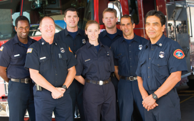 group of firefighters posing happily in front of a firetruck