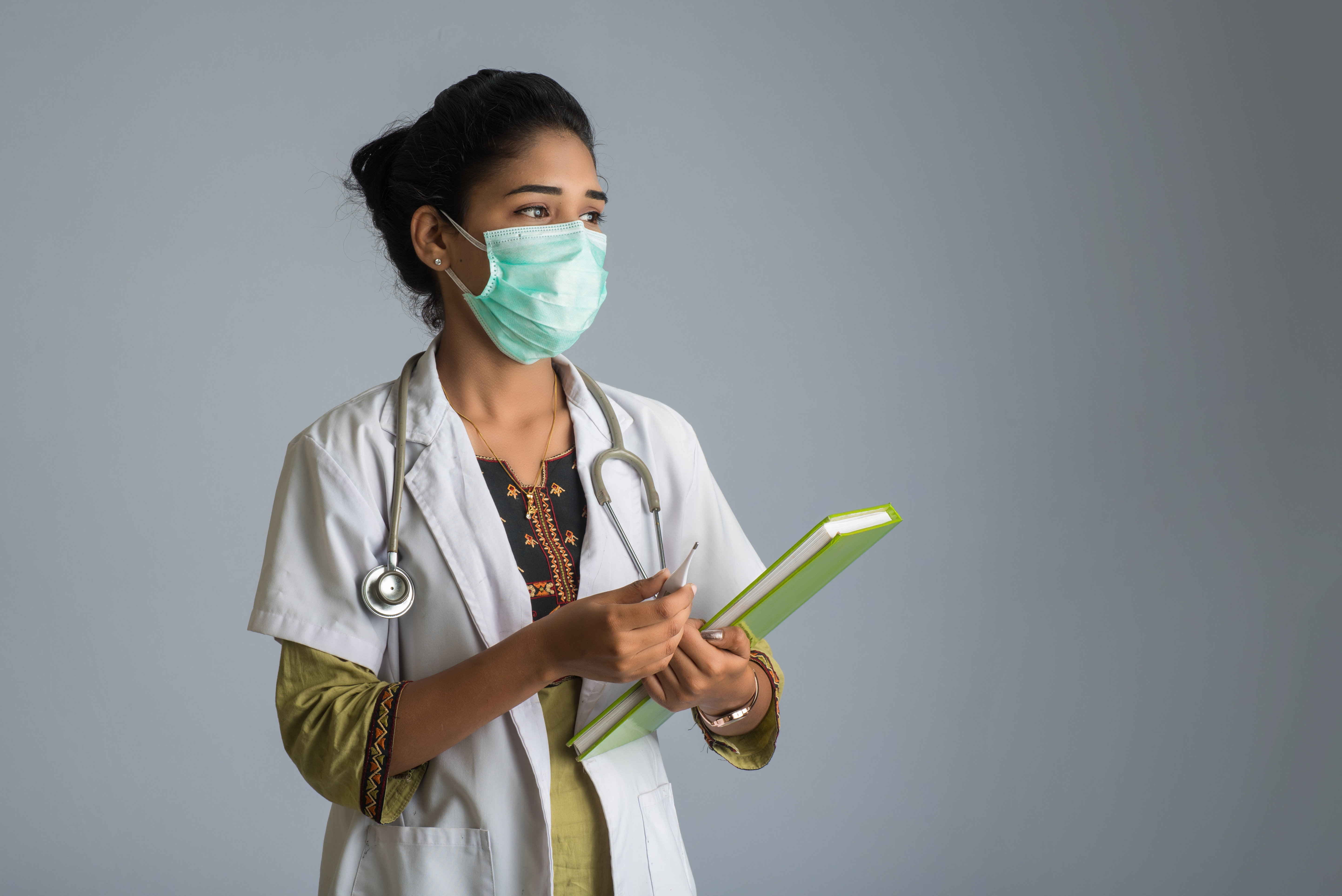 female doctor standing, holding her chart, with surgical mask on